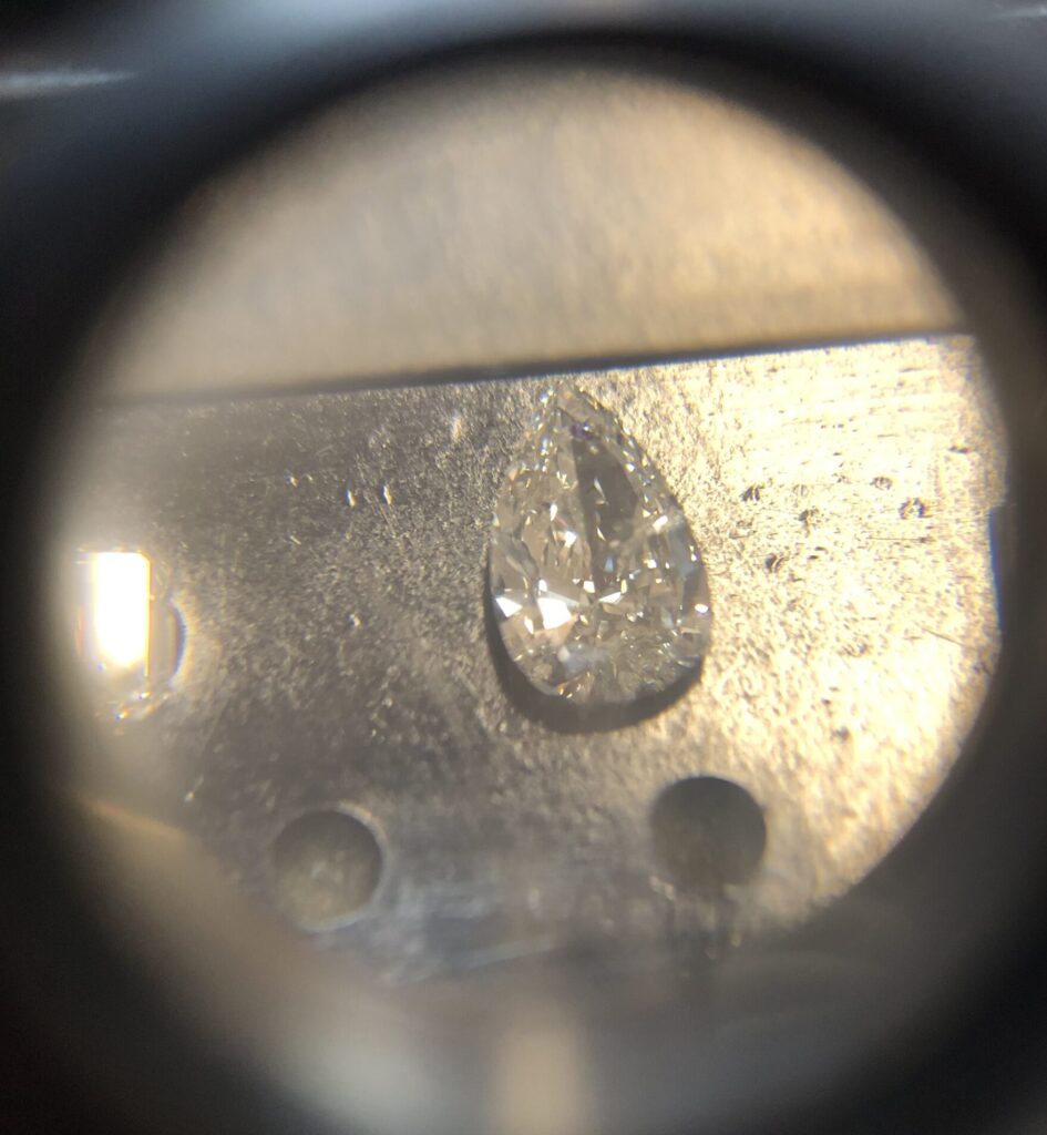 Een diamant van peer-vorm gezien onder een microscoop die geplaatst is op een zwarte tentoonstelling doos.
